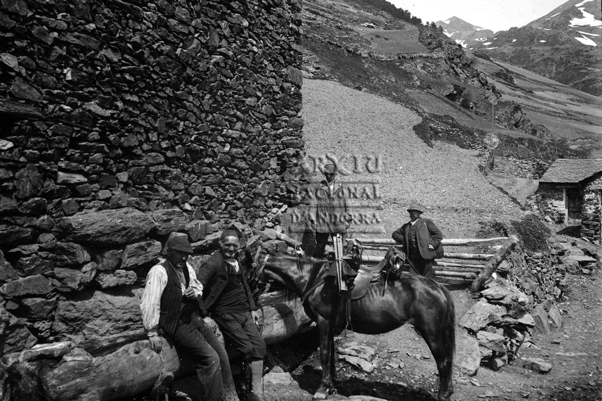 160-FBUI: Instantània d’uns homes asseguts al damunt d’un cóm al davant d’una casa