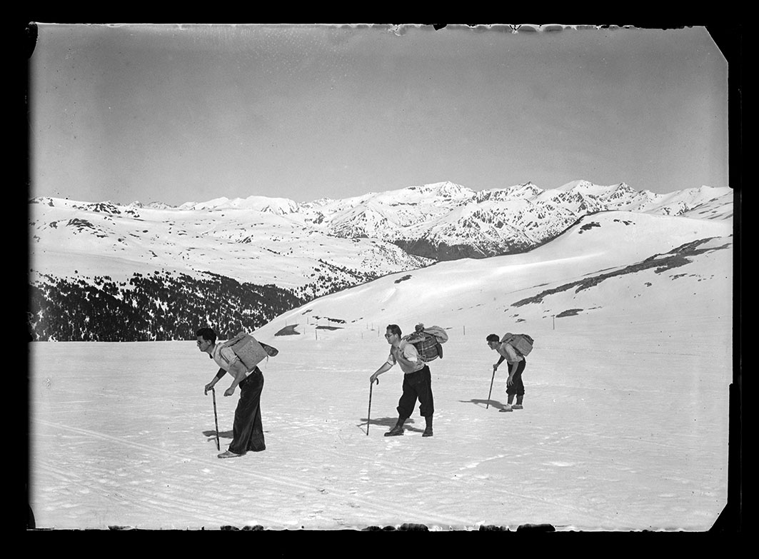 NC_0121: Instantània de tres homes carregats amb fardos pujant caminant pels pendents del port d’Envalira